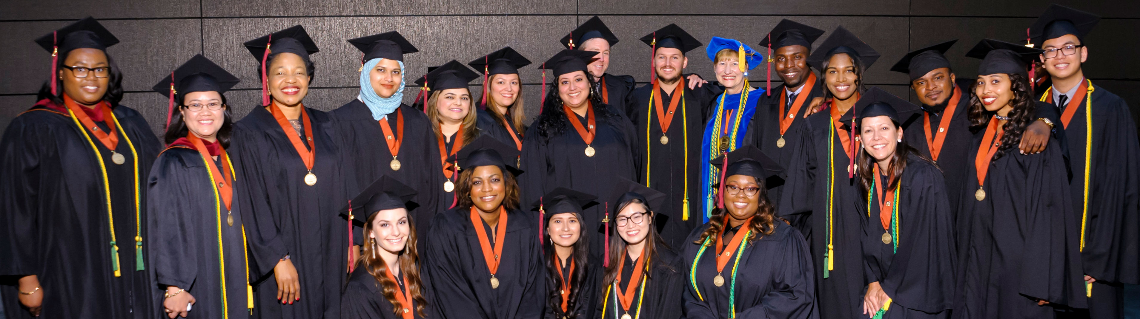 Large group of graduates and their professor smiling and posing in celebration.