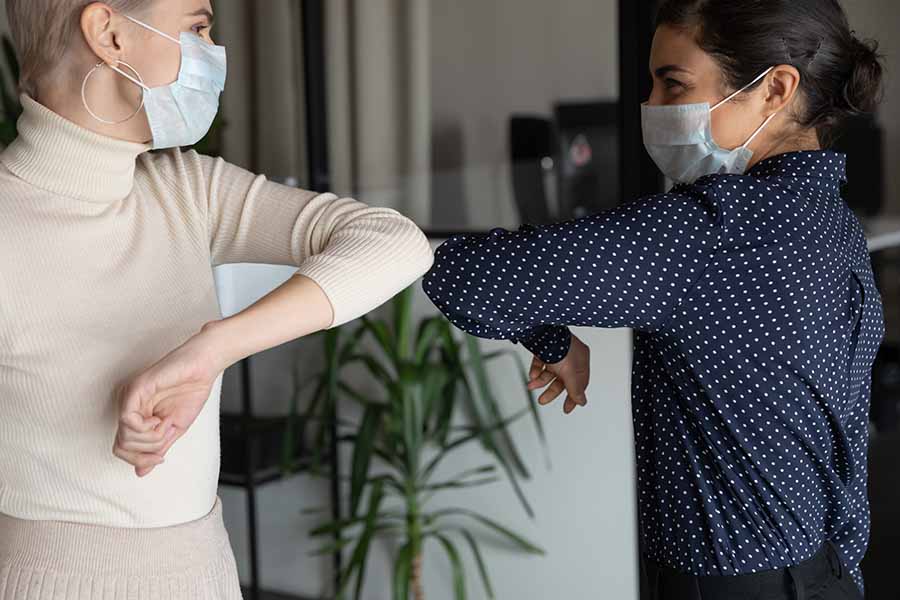 Two females wearing masks bumping elbows