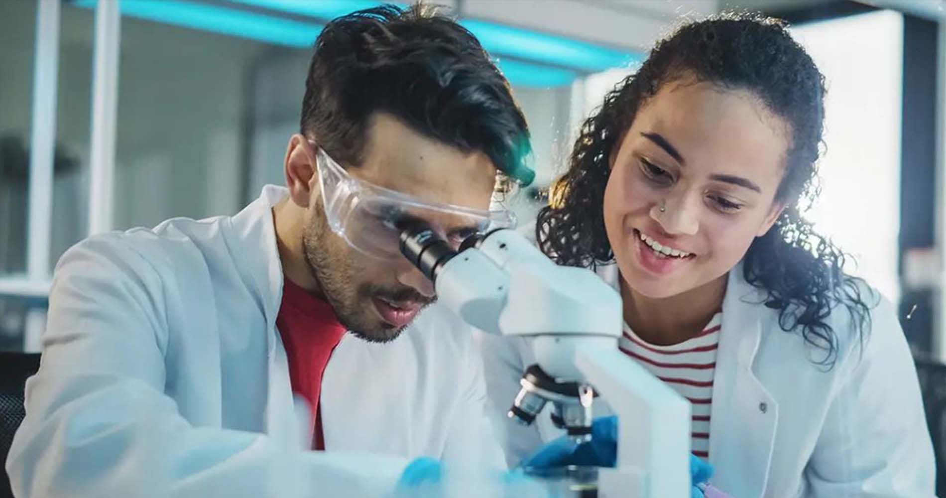 Two students in lab coats looking through a microscope