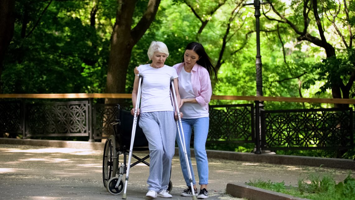 A young woman helps an older woman stand up with the help of crutches
