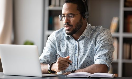 Man intently looks at computer laptop while holding a pen