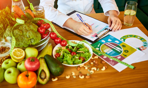 Close up of hands writing notes in front of a variety of fruits and vegetables