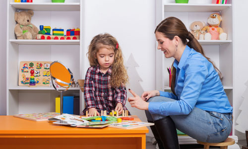 Woman speaks to child in a small chair as child does a motor skills assessment