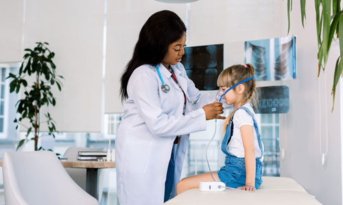Woman puts a respirator mask on a child who sits on a medical examining table